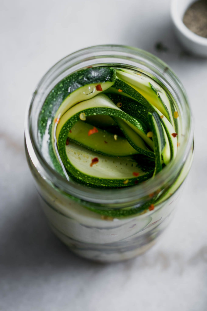 pickled zucchini in a tall glass jar on a white table