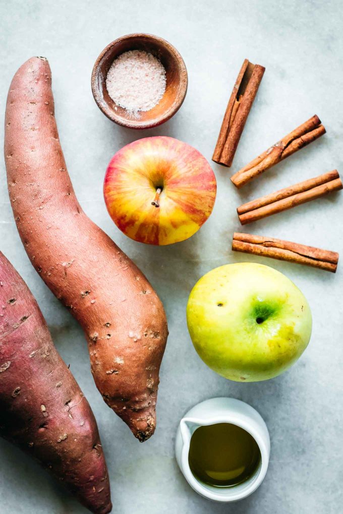 sweet potatoes, apples, cinnamon sticks, and bowls of salt and oil on a marble countertop