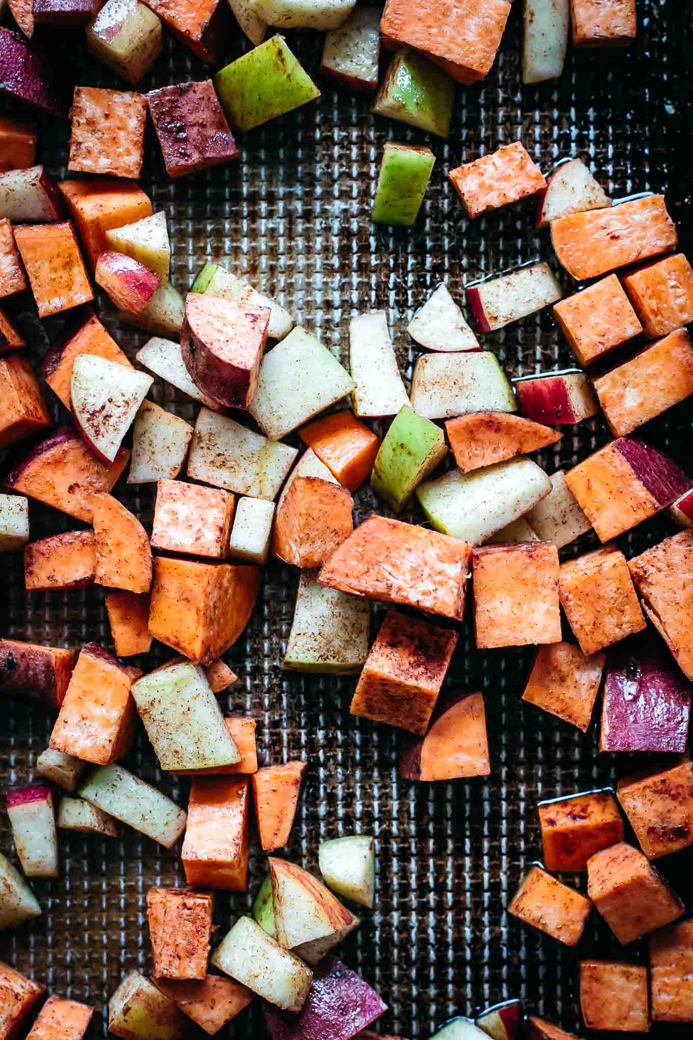 cubed sweet potatoes and apples on a roasting pan before baking