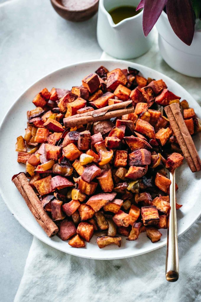 roasted yams and apples with cinnamon sticks on a serving plate on a white table