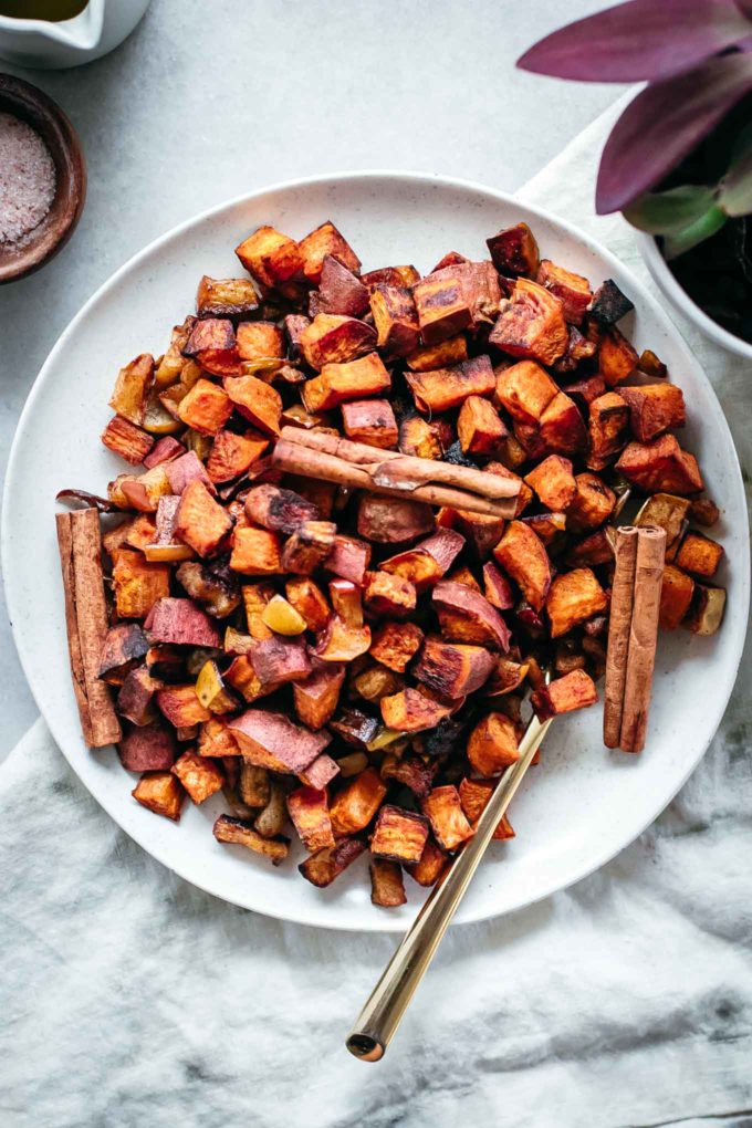 roasted diced sweet potatoes and apples on a white plate with cinnamon sticks