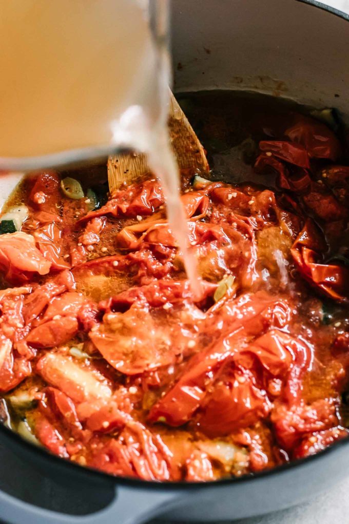 broth pouring into a soup pot with tomatoes