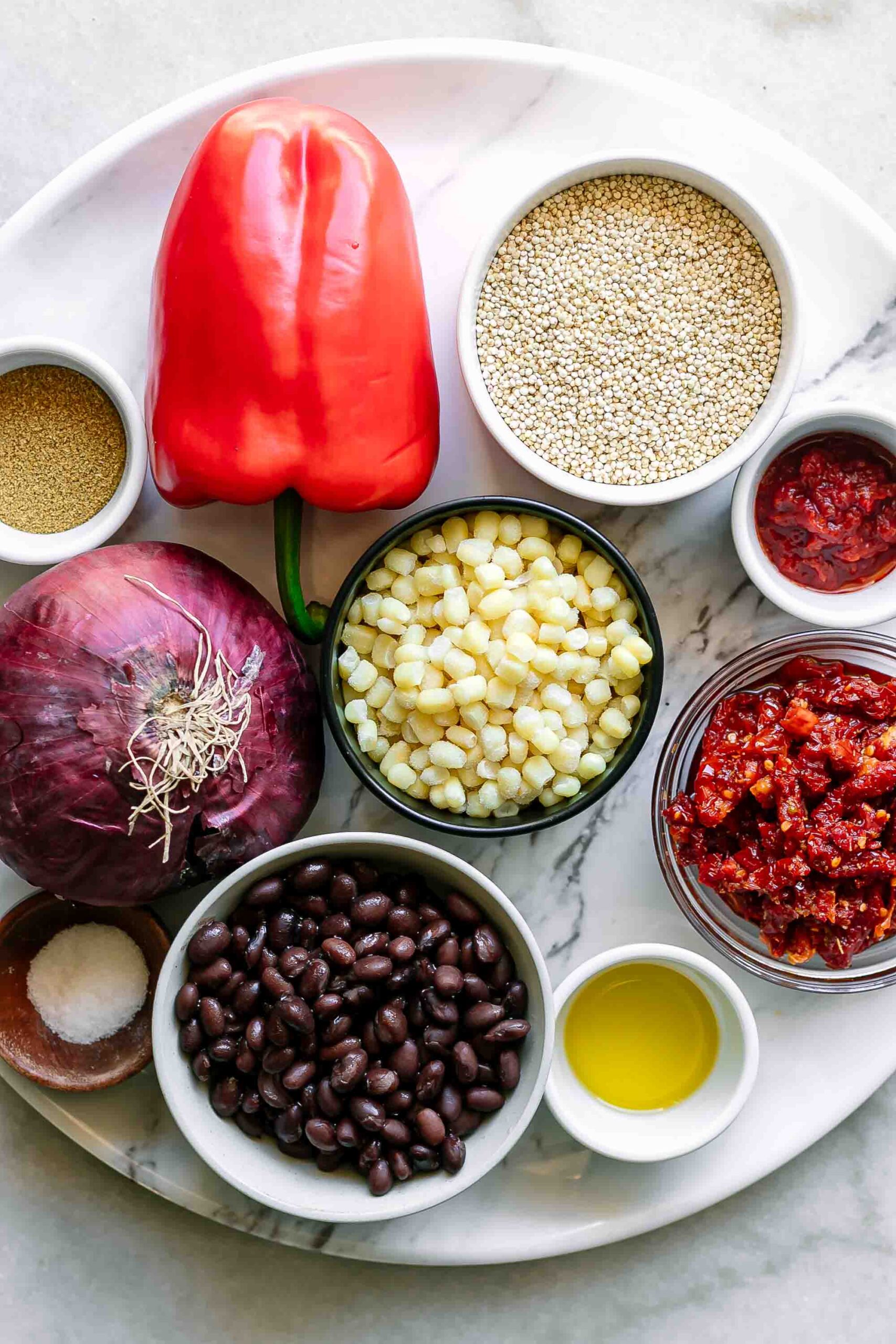 quinoa, black beans, bell pepper, onion, corn, sun-dried tomatoes, and spices on a table for a grain bowl