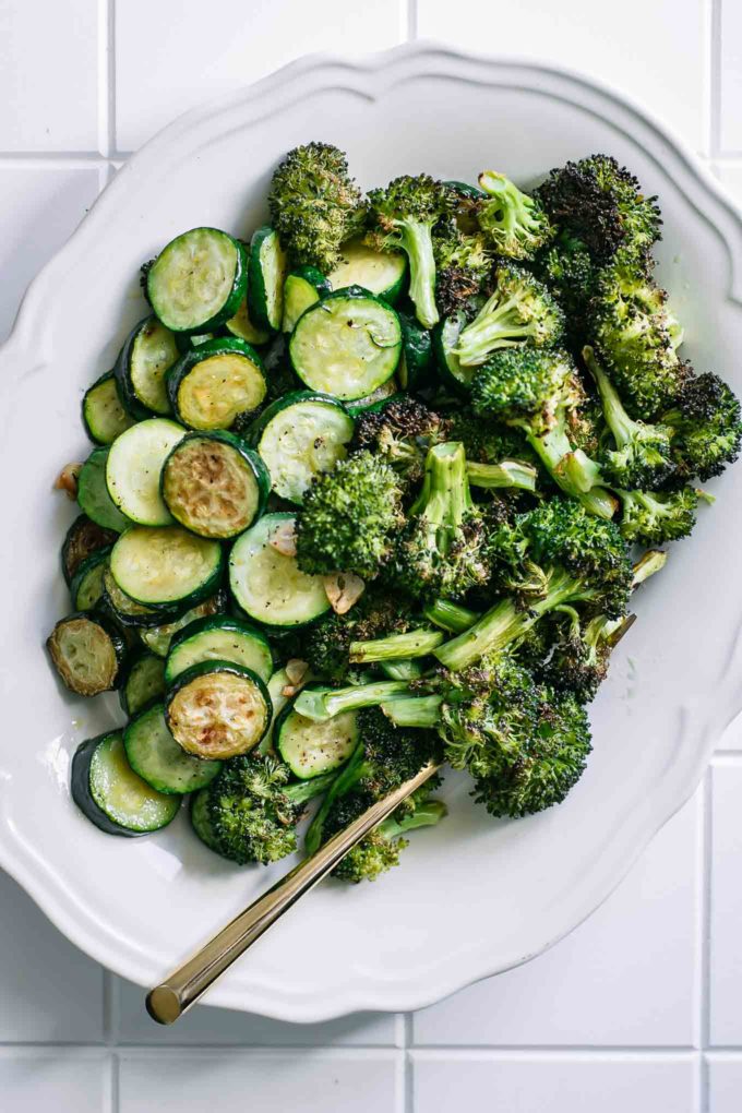 oven roasted broccoli and sliced zucchini on a white plate on a white table