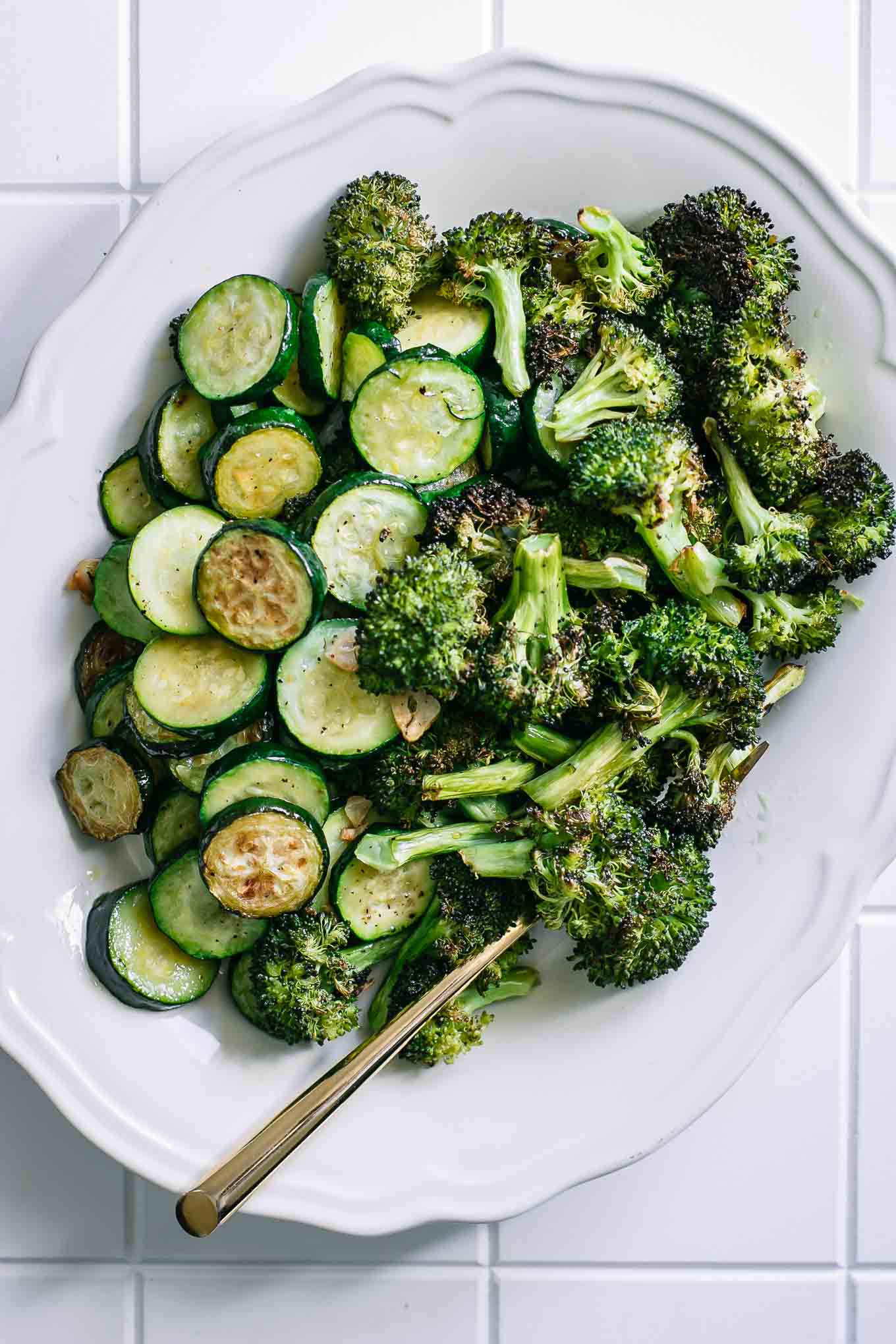 oven roasted broccoli and sliced zucchini on a white plate on a white table