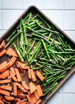roasted cut sweet potatoes and asparagus spears on a baking sheet on a white counter