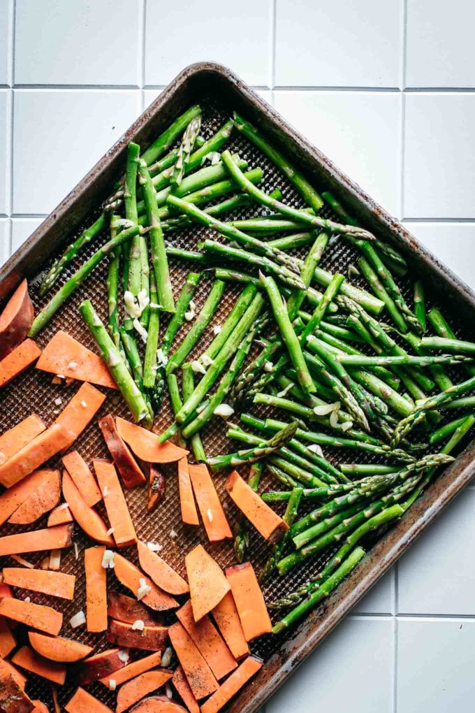 roasted cut sweet potatoes and asparagus spears on a baking sheet on a white counter