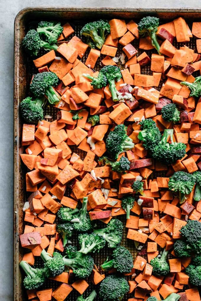 cut sweet potatoes and broccoli on a sheet pan before roasting