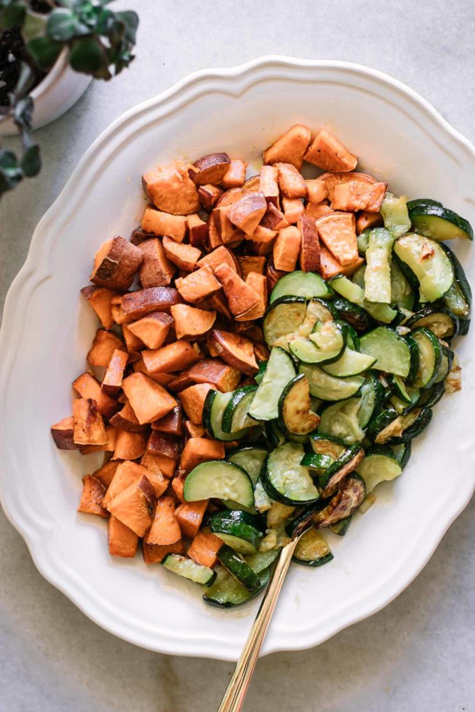 roasted cut sweet potatoes and zucchini on a white plate with a gold fork