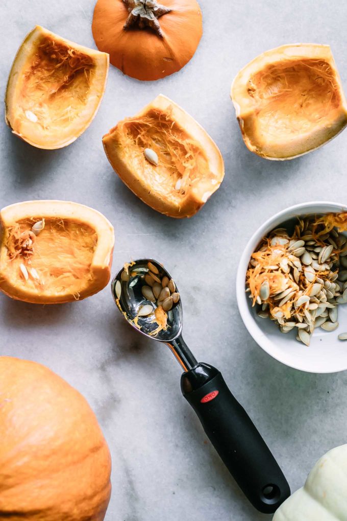 a metal scoop next to small pieces of pumpkin and a small bowl containing fresh pumpkin seeds