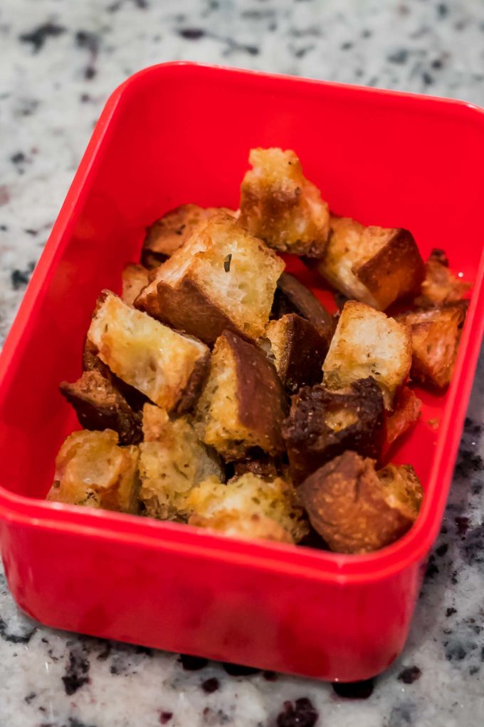 baked croutons in a red storage container on a countertop