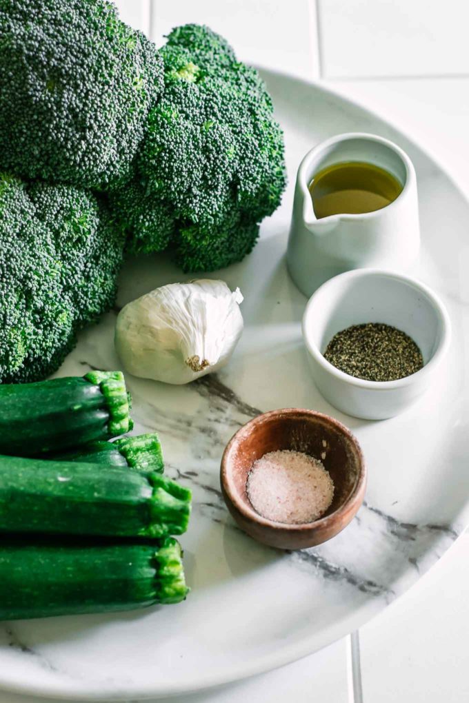 broccoli, zucchini, garlic, and bowls of oil, salt, and pepper on a white countertop