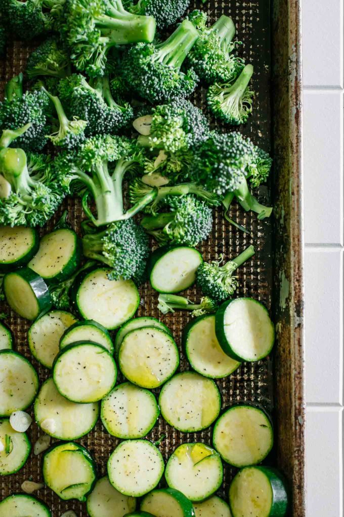 raw broccoli and zucchini slices on a metal baking sheet