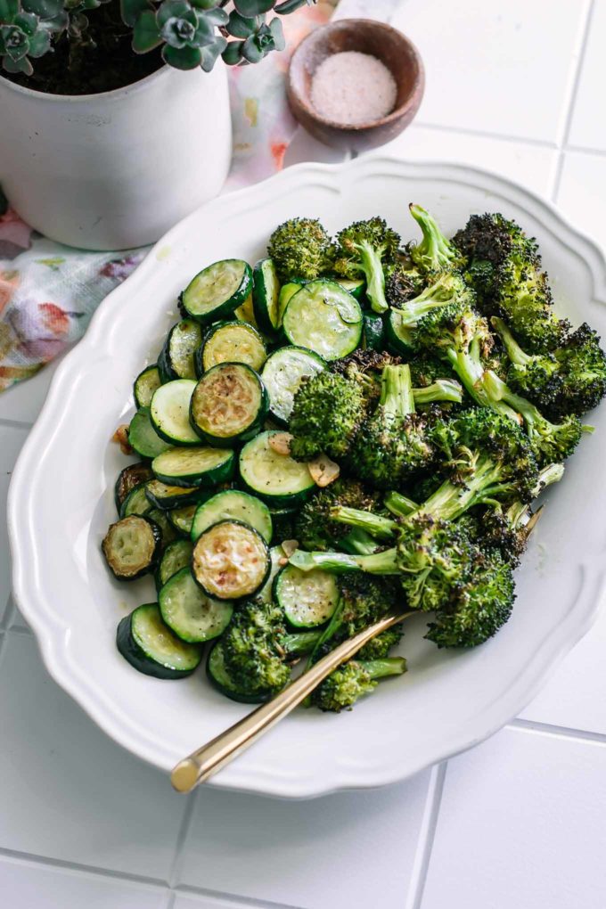 roasted zucchini slices and broccoli florets on a serving platter on a white tiled counter