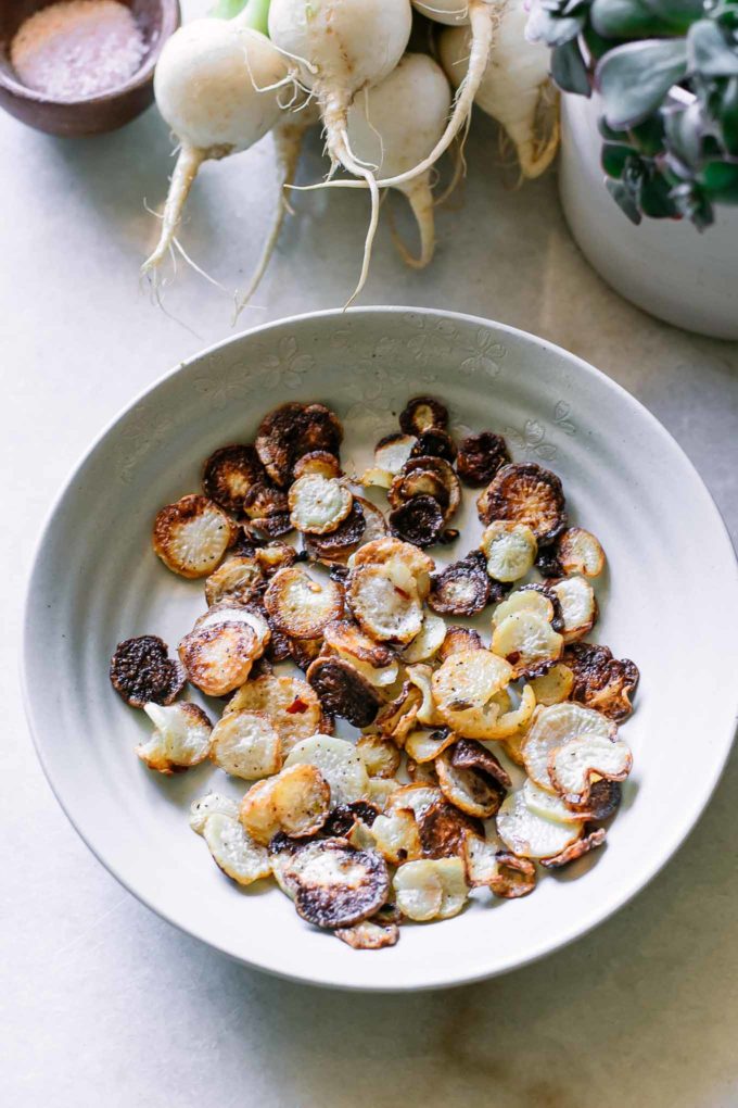 roasted turnip chips in a white bowl with turnips in the background
