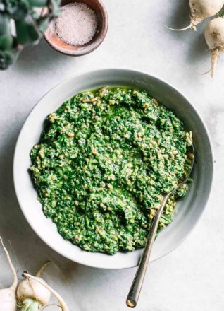 turnip greens pesto in a bowl with a gold spoon on a white marble countertop