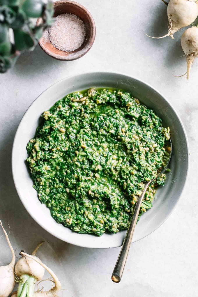 turnip greens pesto in a bowl with a gold spoon on a white marble countertop