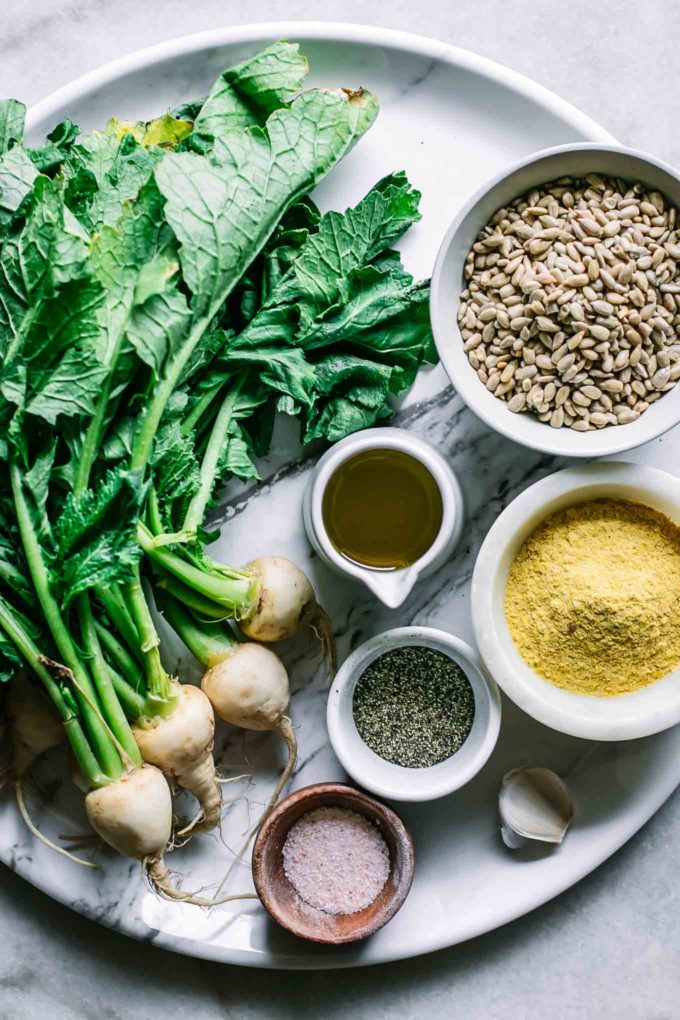 turnips with greens, sunflower seeds, olive oil, nutritional yeast, garlic, salt and pepper on a tray