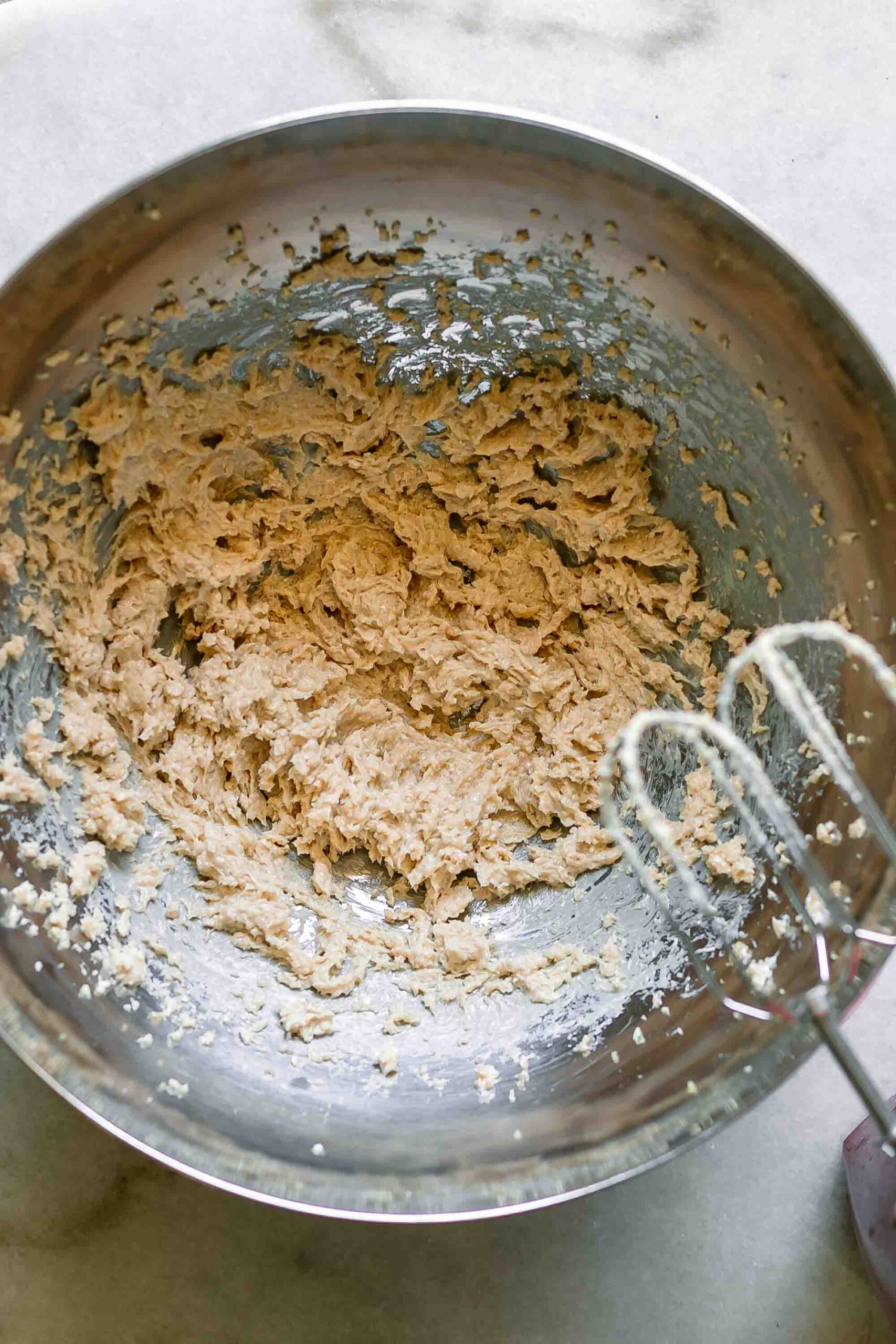 whipped butter with brown sugar in a mixing bowl with a handheld mixer on a white table