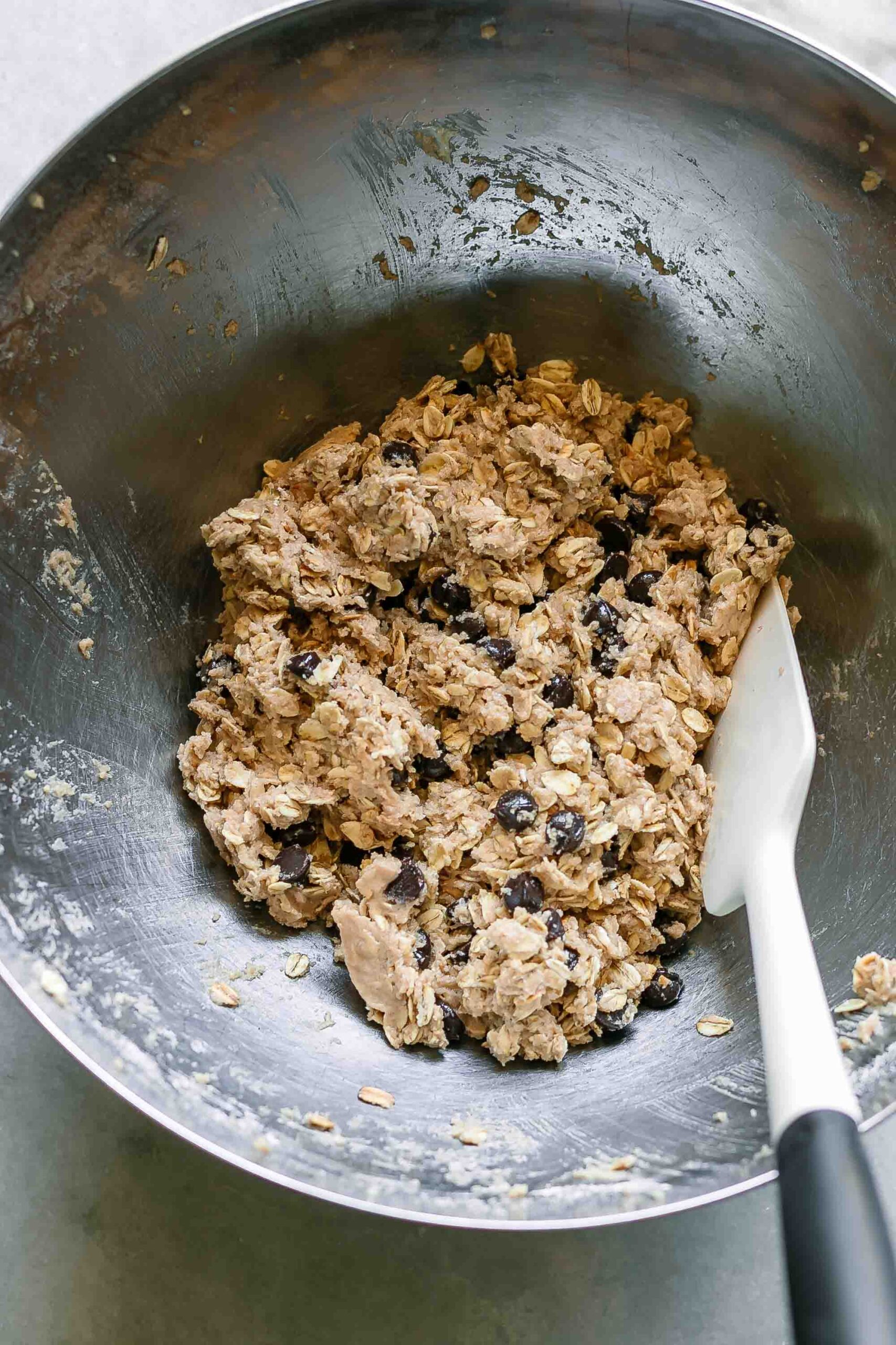 chocolate chip oatmeal cookie batter in a mixing bowl on a white table