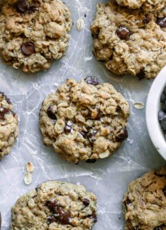 vegan oatmeal chocolate chip cookies on a white table with a bowl of chocolate chips