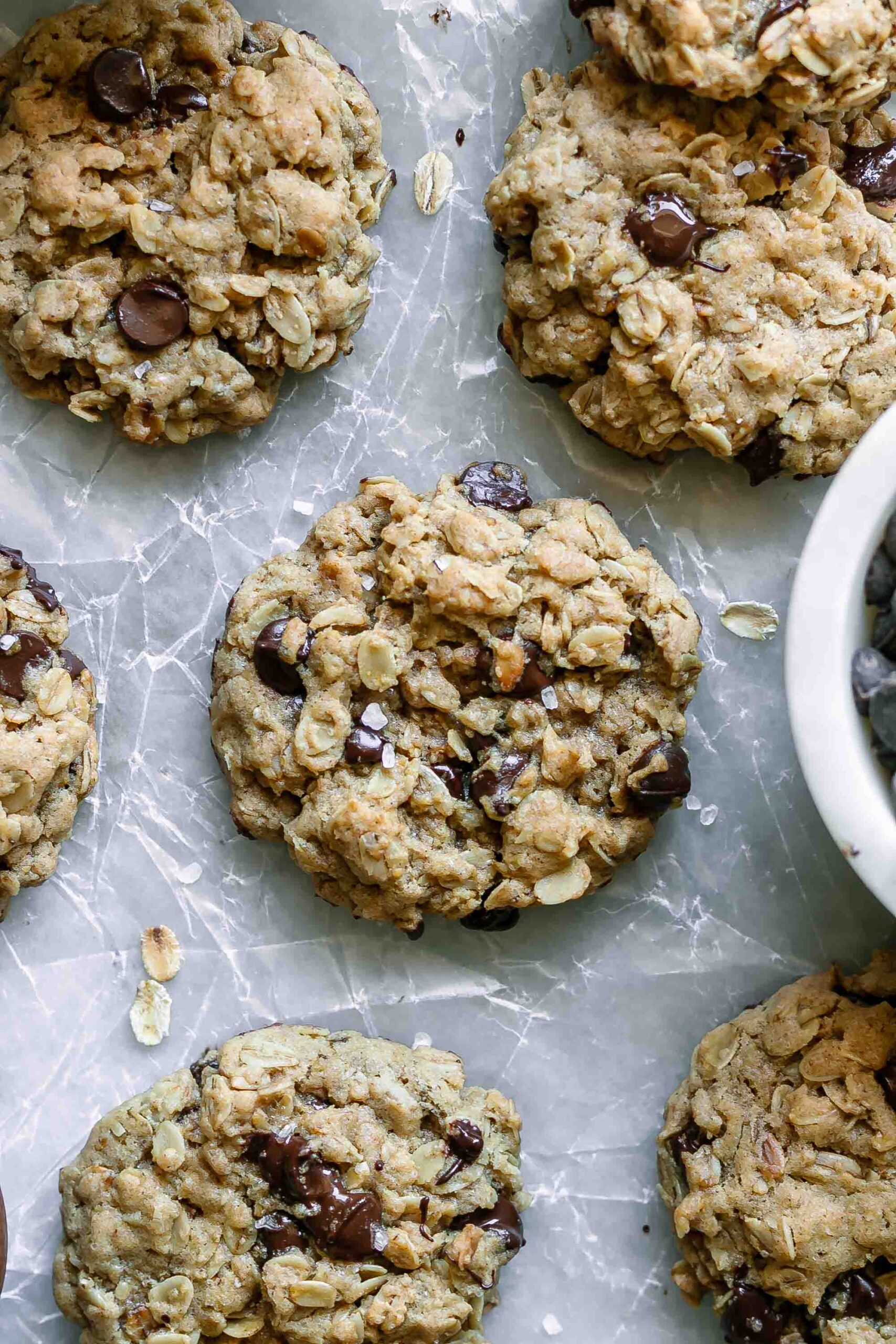 vegan oatmeal chocolate chip cookies on a white table with a bowl of chocolate chips