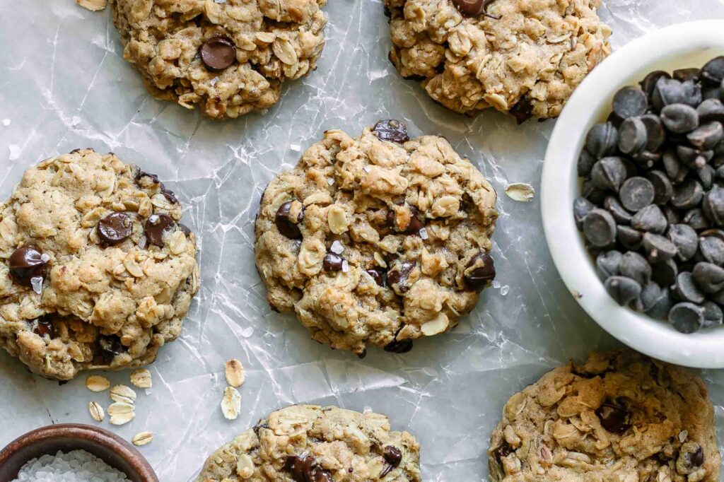 vegan oatmeal chocolate chip cookies on a white table with a bowl of chocolate chips