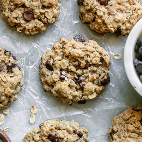 vegan oatmeal chocolate chip cookies on a white table with a bowl of chocolate chips