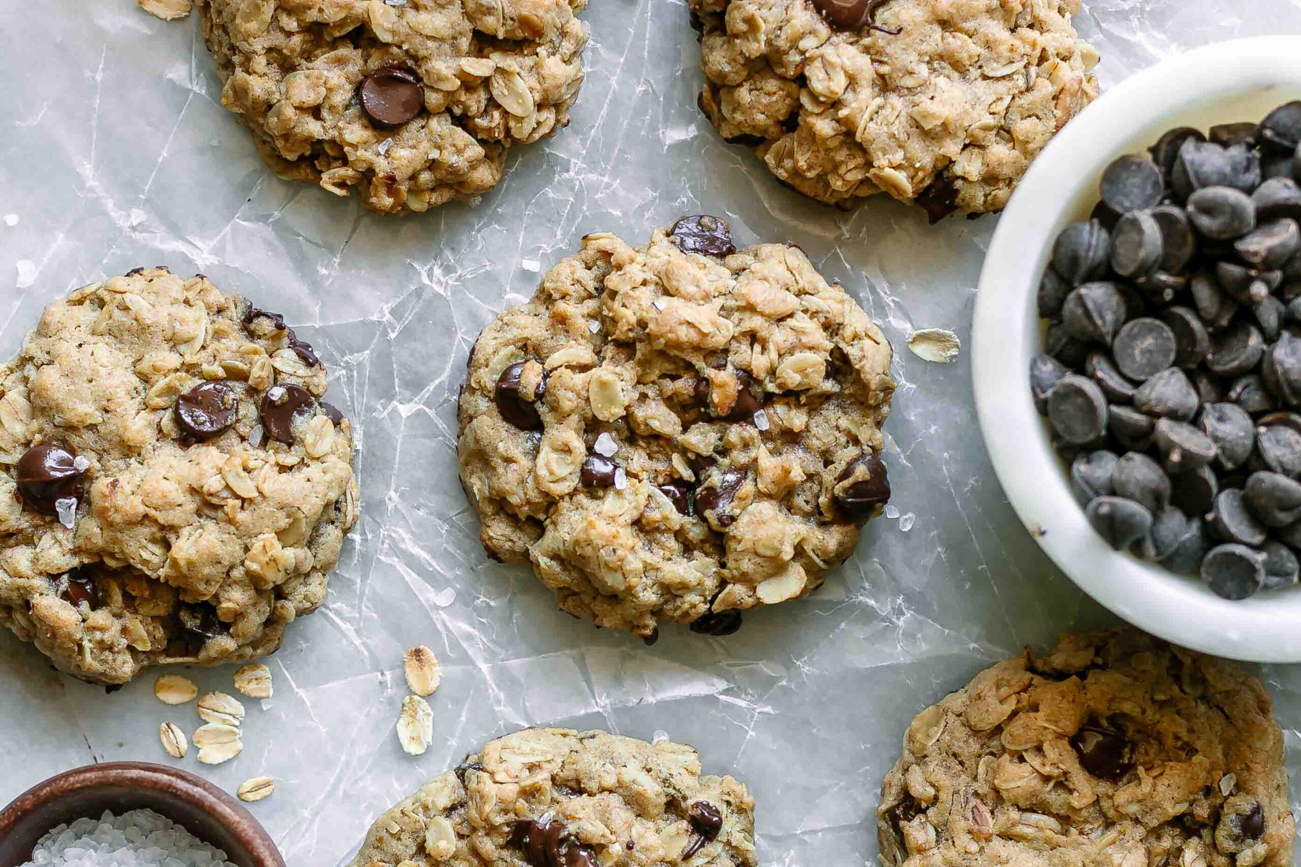 vegan oatmeal chocolate chip cookies on a white table with a bowl of chocolate chips