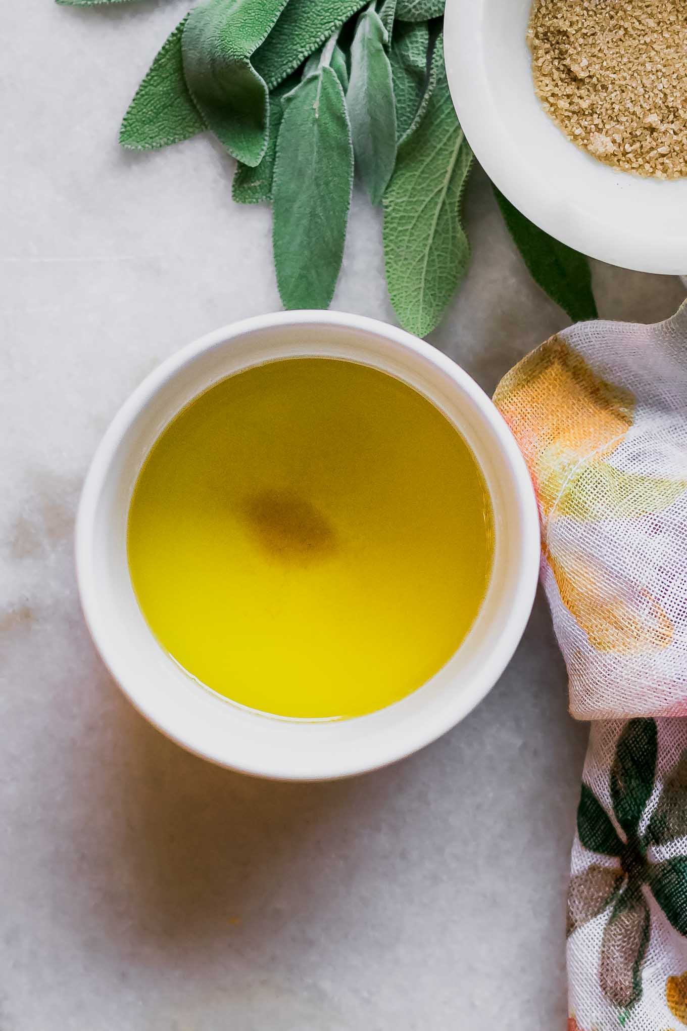 a bowl of brown sugar, sage, and butter sauce in a white ramekin on a white table with fresh sage leaves