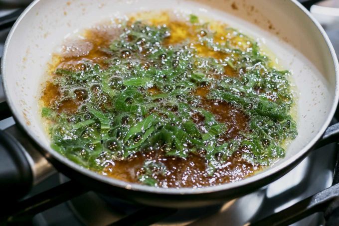 brown sugar and butter sauce with sage leaves simmering in a sauce pan on a stovetop