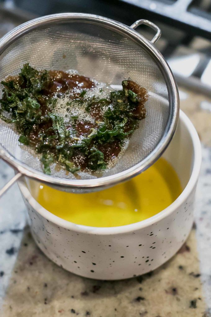 sage butter sauce straining through a sieve into a white ramekin