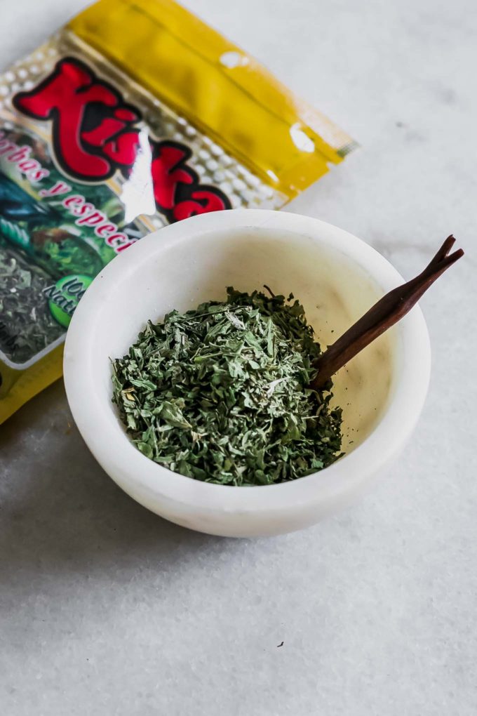 a small bowl of dried guacas herb on a white table with a guascas herb packet in the background