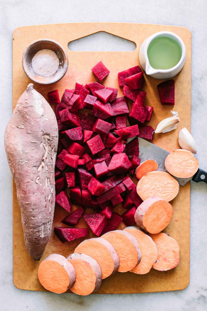 a wood cutting board with cut sweet potatoes and beets