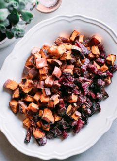 a white plate with roasted sweet potatoes and beets on white table