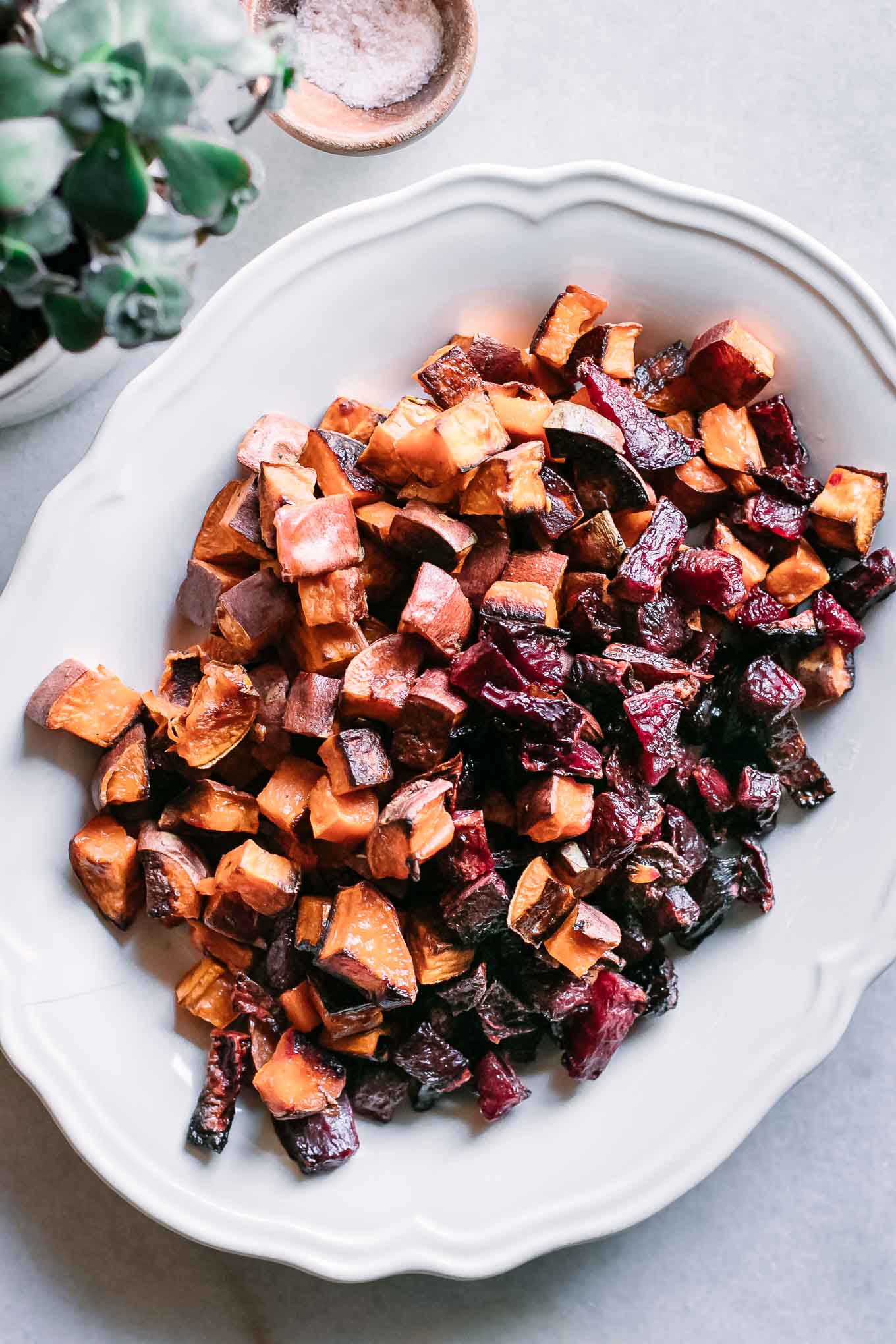 a white plate with roasted sweet potatoes and beets on white table