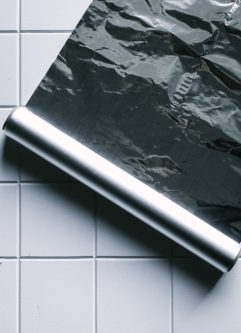 a roll of aluminum foil rolled out on a white tile countertop