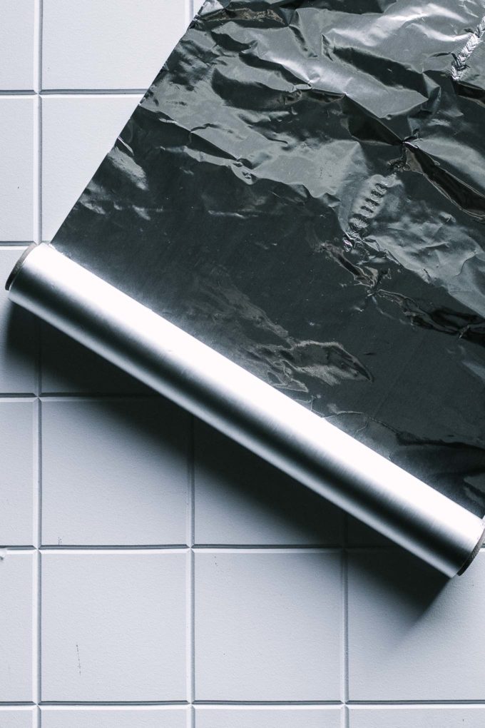 a roll of aluminum foil rolled out on a white tile countertop