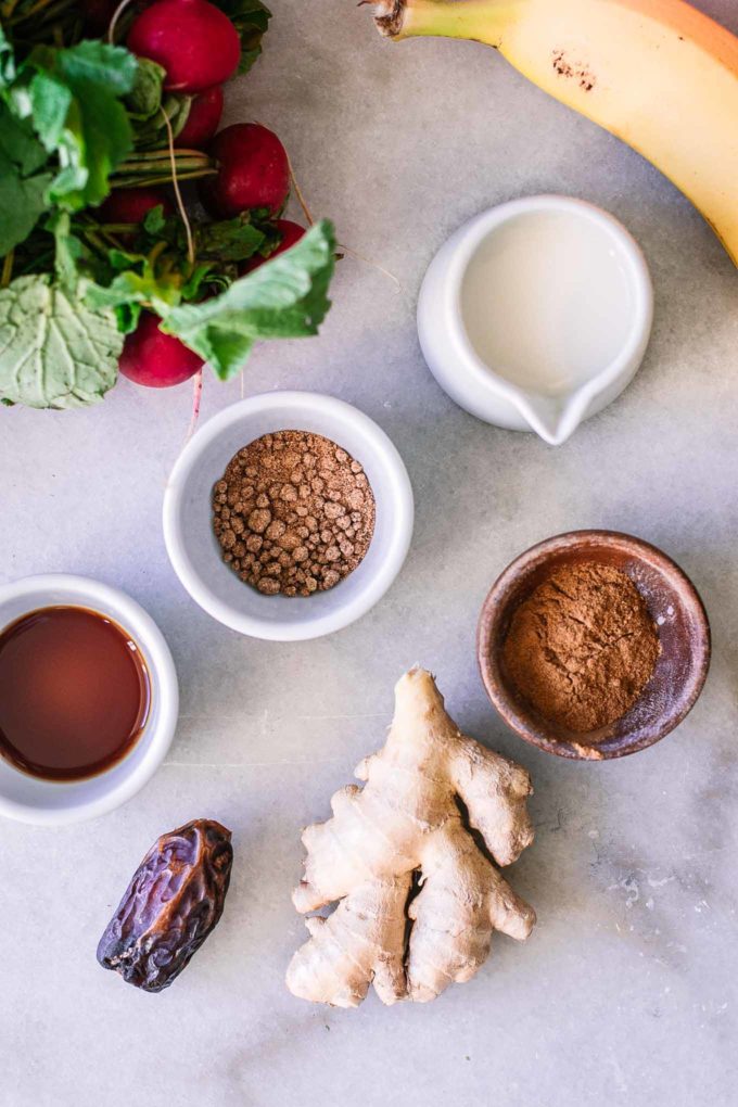 radishes, banana, oat milk, spices, ginger, and dates on a marble table