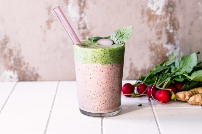 a radish and radish greens layered smoothie in a glass with a straw on a white table with fresh radishes