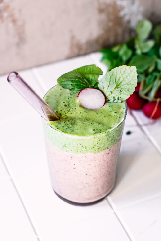 a radish greens smoothie in a glass with a glass straw