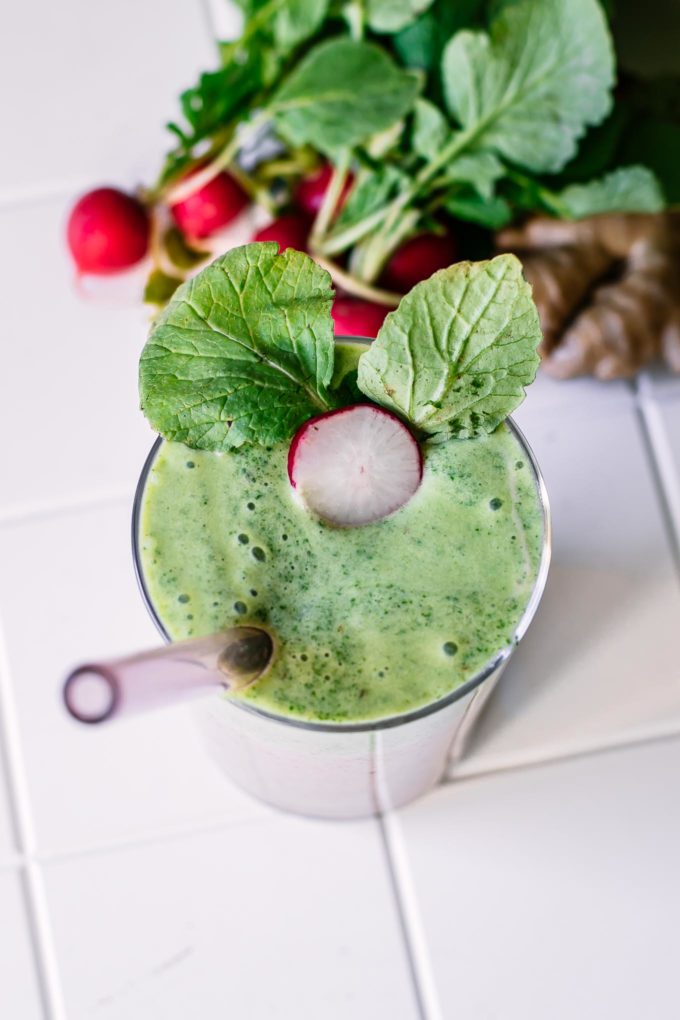 a top down photo of a green smoothie made with radishes with a radish slice and radish leaf garnish