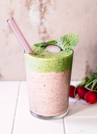 a pink and green smoothie made with leftover radish greens on a white table with a glass straw
