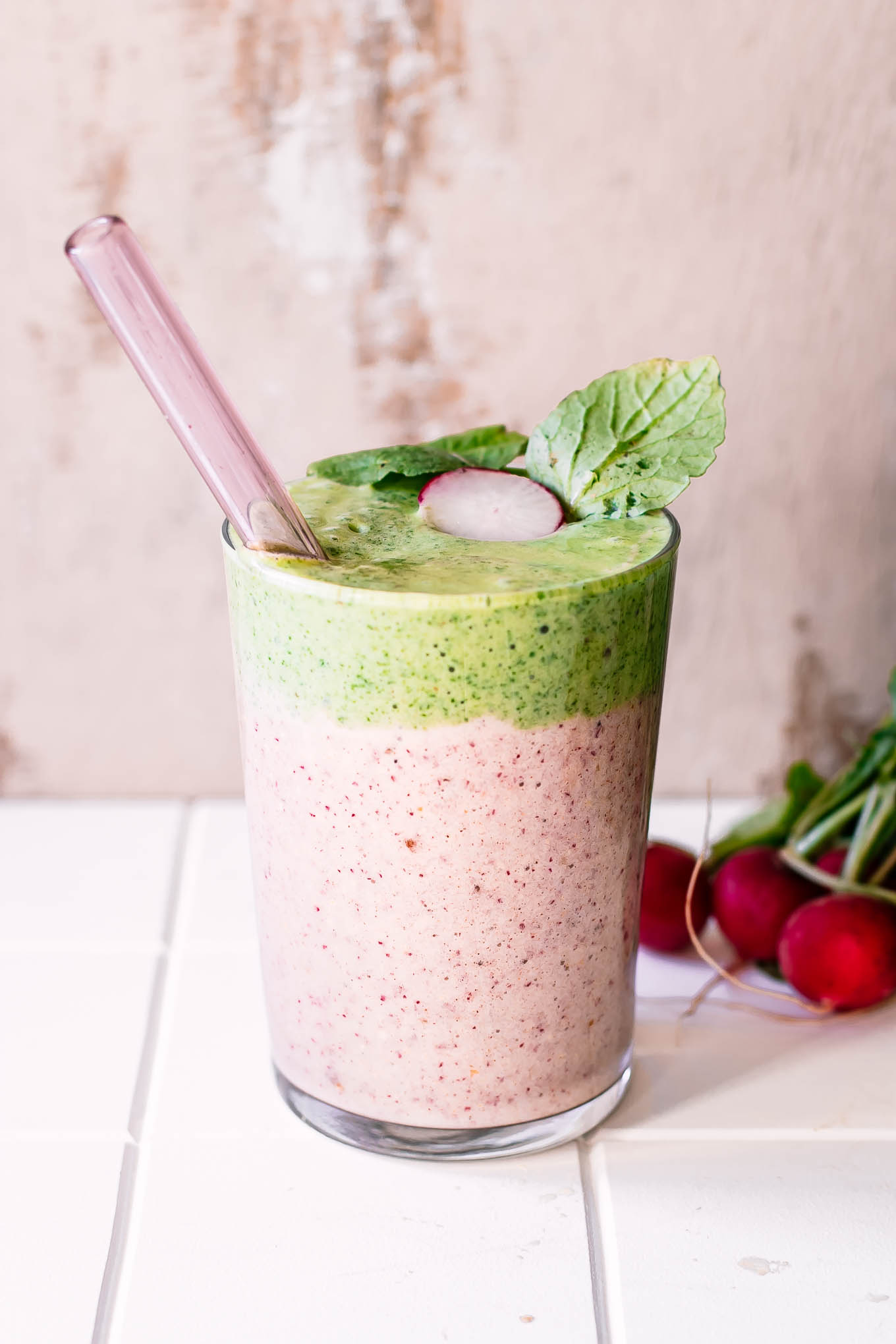 a pink and green smoothie made with leftover radish greens on a white table with a glass straw