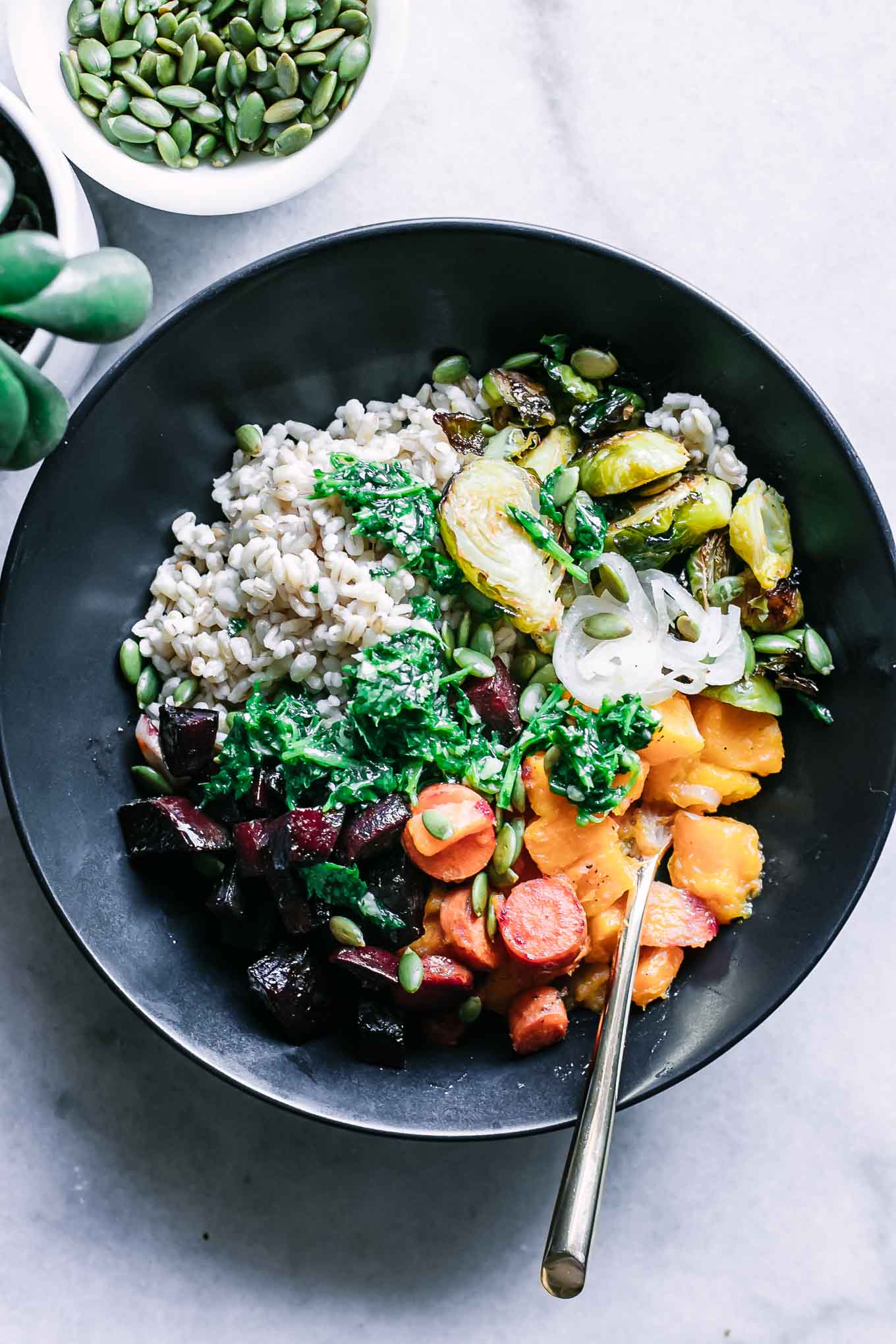 a black bowl containing roasted vegetable barley ingredients with a gold spoon