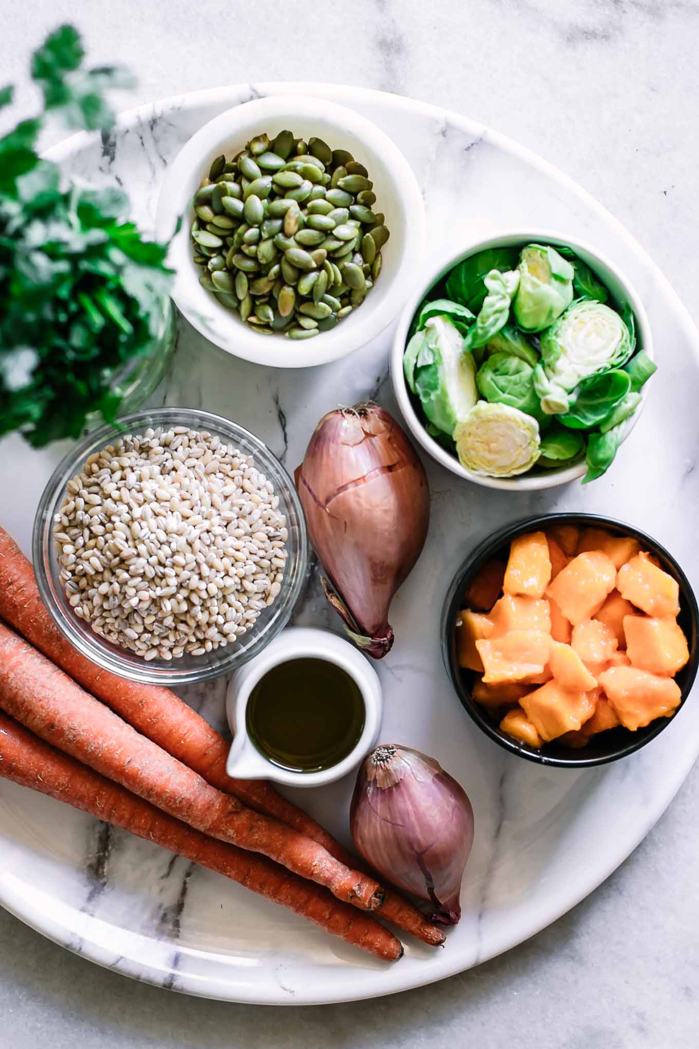 a platter with carrots, shallots, brussels sprouts, squash, barley, pumpkin seeds and olive oil