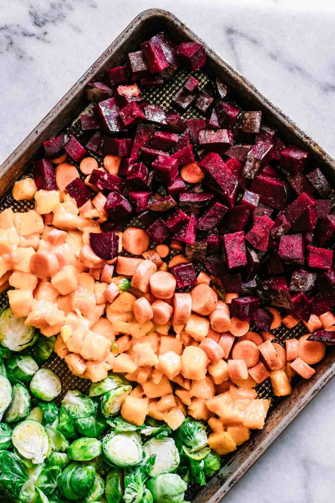 a baking sheet with sliced and seasoned beets, carrots and brussels sprouts