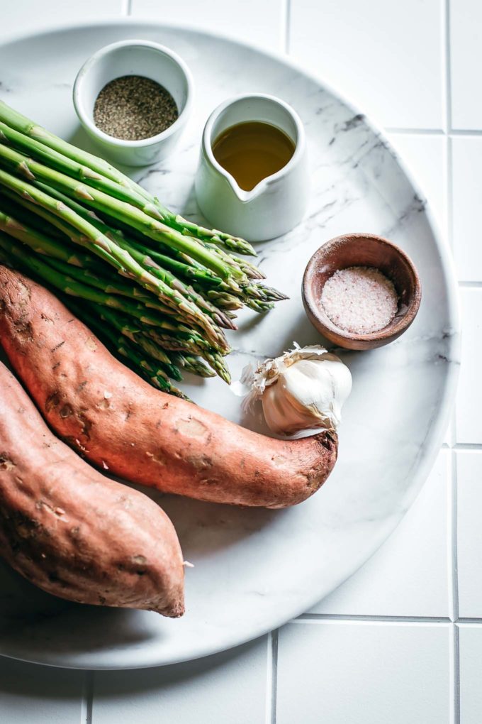 sweet potatoes, asparagus, and bowls of olive oil, salt, and pepper on a white table