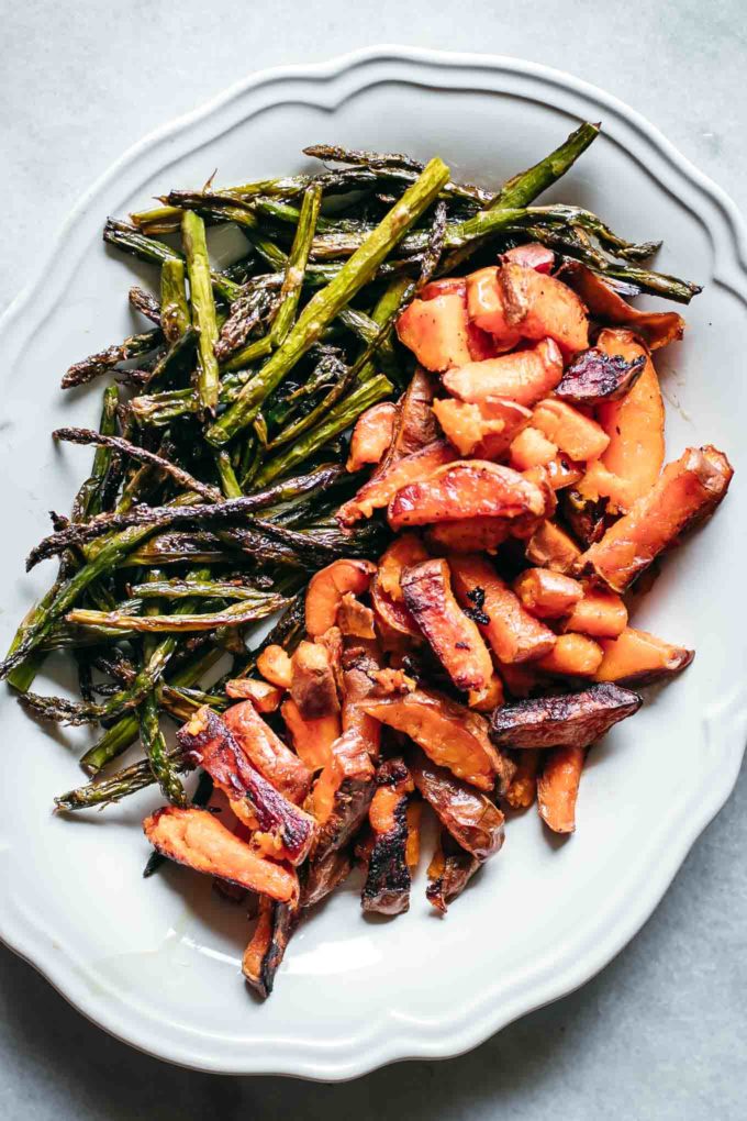 baked asparagus spears and sliced sweet potatoes on a white serving dish