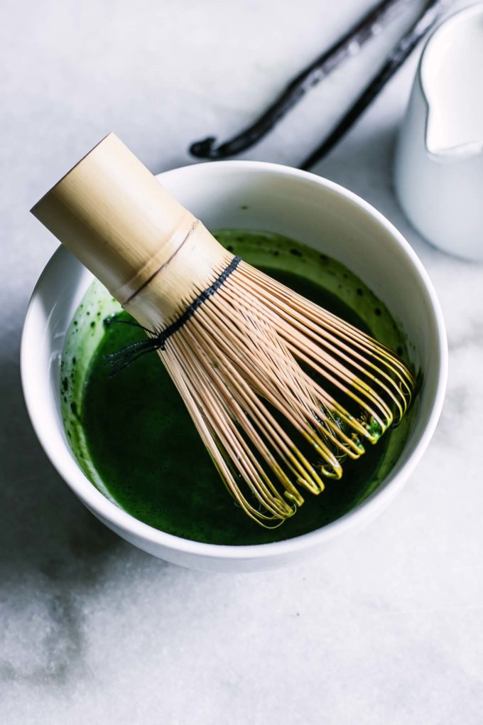a matcha whisk inside a small white bowl with matcha powder on a white table